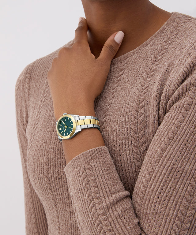 Person wearing a two-tone watch with a green face on a plain background