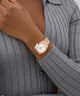 Rose gold GUESS Ladies Rose Gold Tone Date Watch on a wrist with a gray sweater