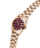 GUESS Ladies Rose Gold Tone Date Watch with a burgundy face on a white background lifestyle