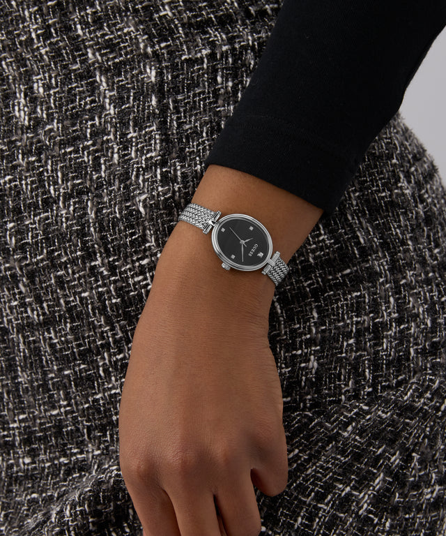 GUESS Ladies Silver Tone Analog Watch on a wrist with a textured black and white background
