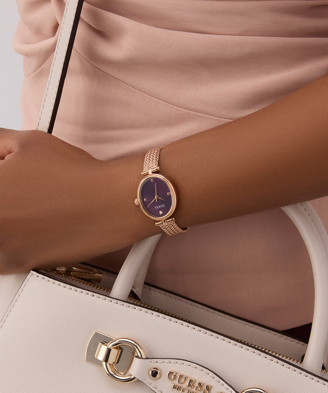 GUESS Ladies Rose Gold Tone Analog Watch on a wrist with a beige handbag featuring a visible brand logo.