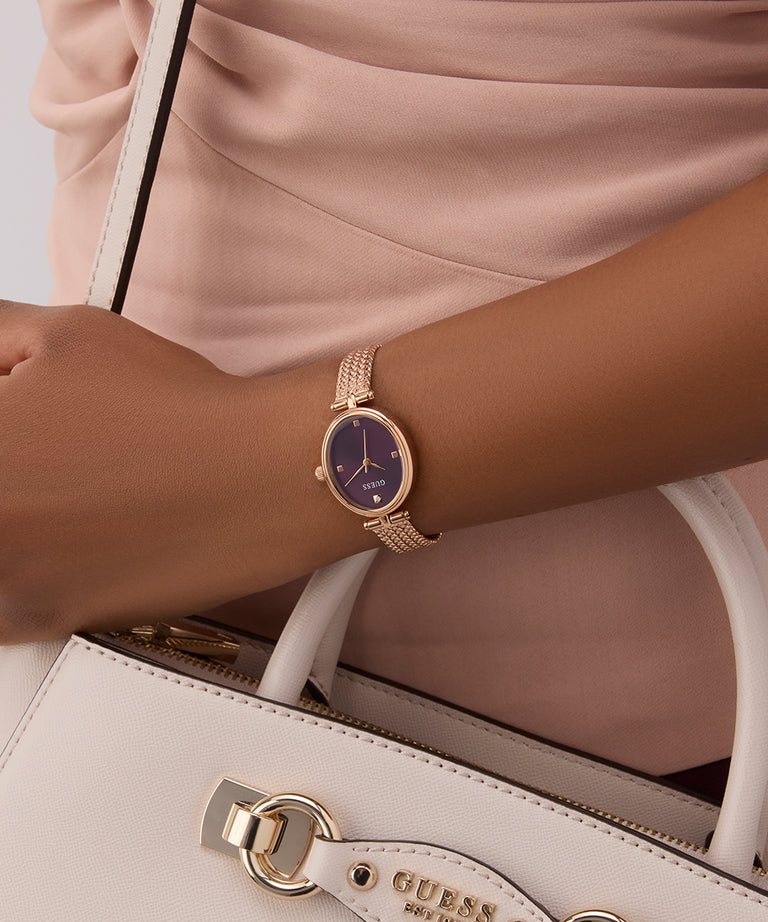 GUESS Ladies Rose Gold Tone Analog Watch on a wrist with a beige handbag featuring a visible brand logo.
