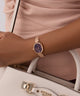 GUESS Ladies Rose Gold Tone Analog Watch on a wrist with a beige handbag featuring a visible brand logo.