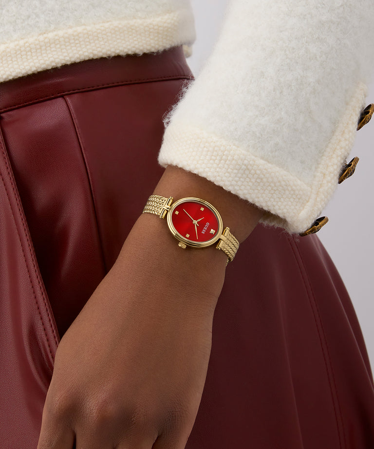 GUESS Ladies Gold Tone Analog Watch with a red face on a wrist, wearing a white coat and maroon skirt.