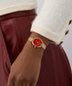 GUESS Ladies Gold Tone Analog Watch with a red face on a wrist, wearing a white coat and maroon skirt.