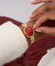 GUESS Ladies Gold Tone Analog Watch with a red face on a wrist, worn by a person in a white sweater.