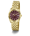 A gold-tone wristwatch with a fluted bezel, gold metal bracelet, and a deep burgundy dial with diamond hour markers and a date window at 3 o'clock. The brand name 'GUESS' is clearly visible on the dial.