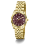 A gold-tone wristwatch with a fluted bezel, gold metal bracelet, and a deep burgundy dial with diamond hour markers and a date window at 3 o'clock. The brand name 'GUESS' is clearly visible on the dial.