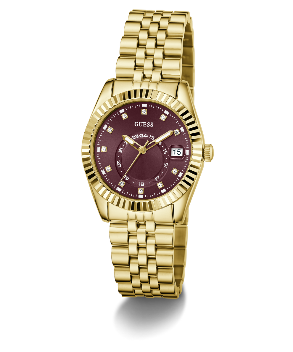A gold-tone wristwatch with a fluted bezel, gold metal bracelet, and a deep burgundy dial with diamond hour markers and a date window at 3 o'clock. The brand name 'GUESS' is clearly visible on the dial.