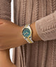 Gold and green watch on a wrist with a brown textured background GW0936L3