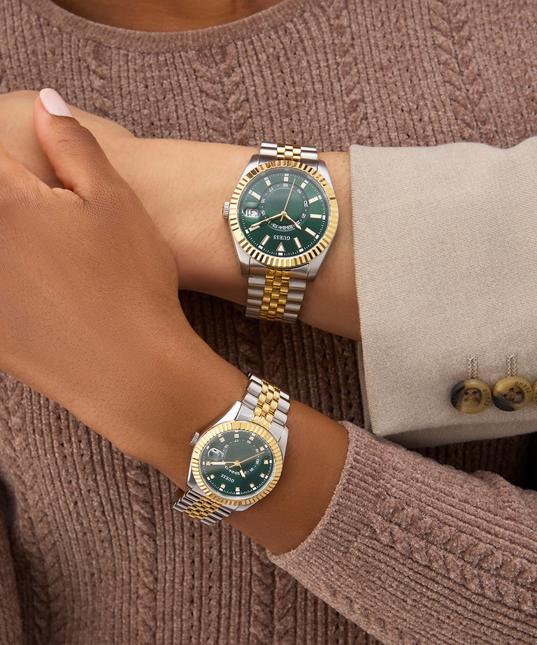 Two gold and green watches on a person's wrist against a brown textured background GW0936L3