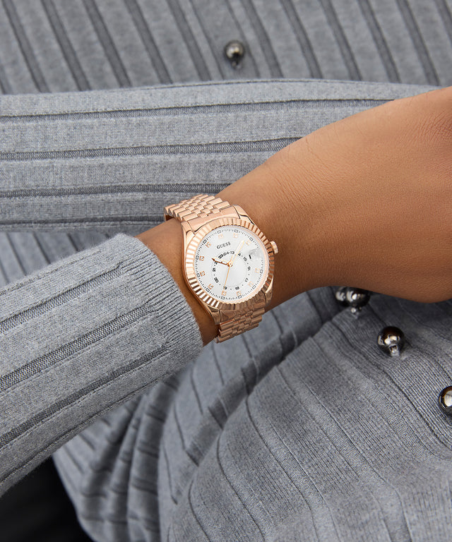 GUESS Ladies Rose Gold Tone Multi-function Date Watch on a wrist with a gray textured background