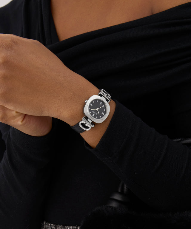 Person wearing a black GUESS Ladies Black Silver Tone Analog Watch with a dark background