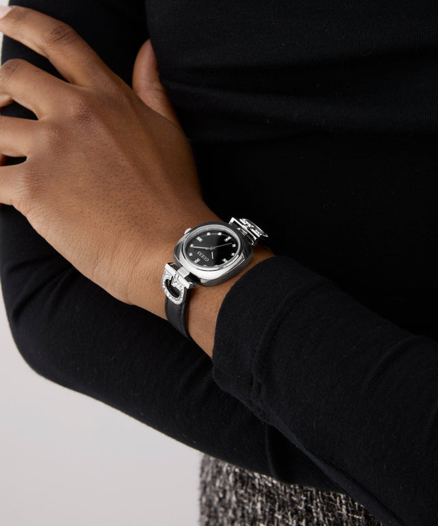 Person wearing a silver GUESS Ladies Black Silver Tone Analog Watch on a plain background