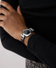 Person wearing a silver GUESS Ladies Black Silver Tone Analog Watch on a plain background