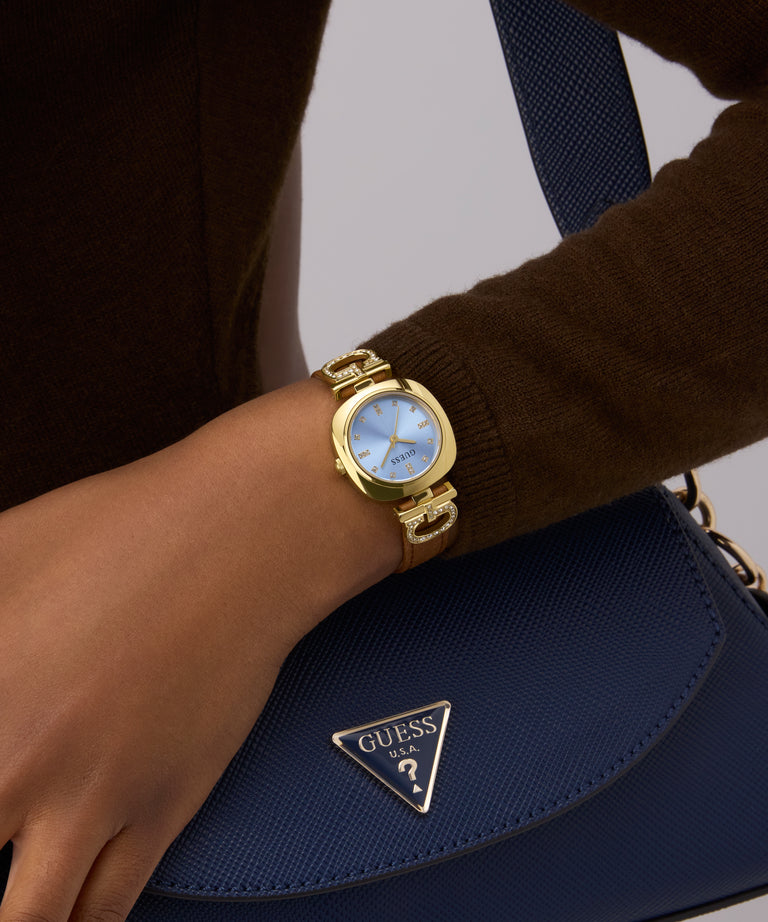 Gold GUESS Ladies Brown Gold Tone Analog Watch on a wrist with a blue handbag featuring a brand logo.