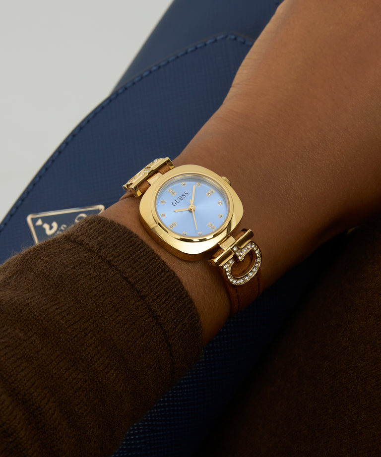 Gold GUESS Ladies Brown Gold Tone Analog Watch on a wrist with a blurred background
