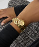 GUESS Ladies Gold Tone Analog Watch on a wrist with a blurred background