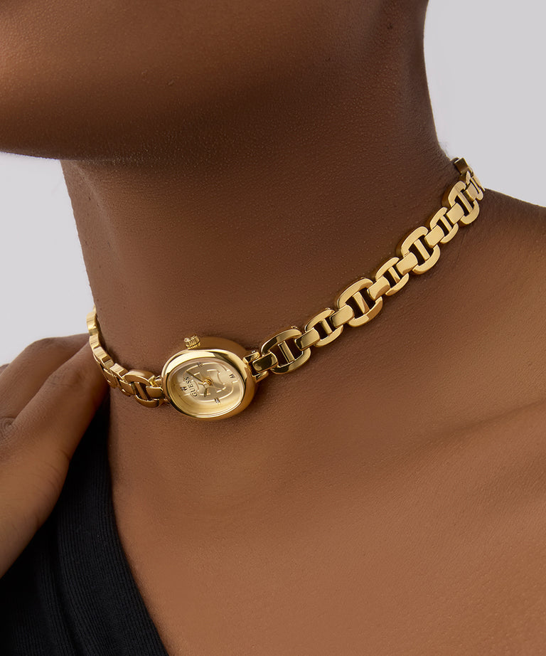 GUESS Ladies Gold Tone Analog Watch with a pendant on a person against a neutral background