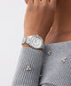 GUESS Ladies Silver Tone Analog Watch on a wrist with a gray sweater and decorative earrings against a light background