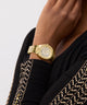 GUESS Ladies Gold Tone Analog Watch on a person's wrist with a black garment featuring gold patterns.