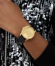 GUESS Ladies Black Gold Tone Analog Watch on a wrist with a sequined background