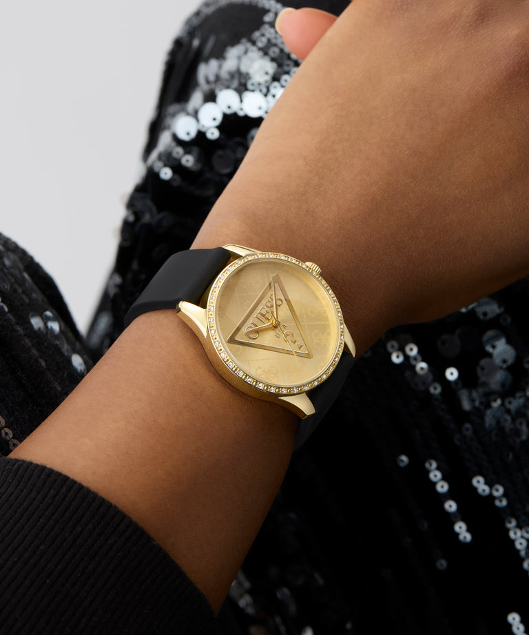 GUESS Ladies Black Gold Tone Analog Watch with a triangle design on a wrist against a black sequined background
