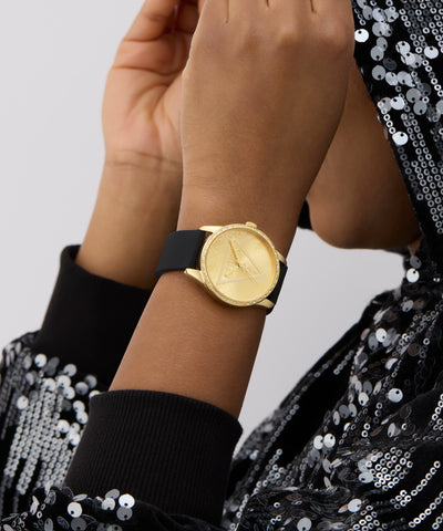 Gold watch on a wrist with a black and silver sequin outfit against a light gray background