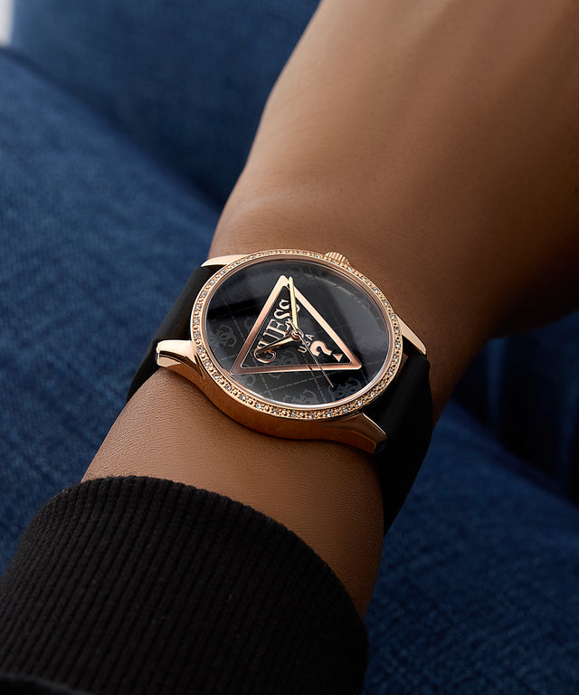 Wrist wearing a rose gold and black watch with a brand logo on a dark background