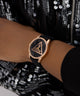 GUESS Ladies Black Rose Gold Tone Analog Watch with black strap on a wrist against a sequined background