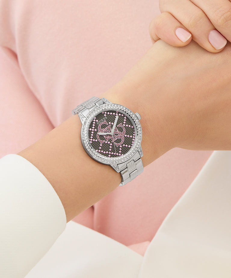 GUESS Ladies Silver Tone Analog Watch with pink accents on a wrist against a light pink background