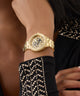 Gold watch on a wrist with a black and gold studded garment