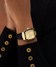 Gold watch on a wrist with a black strap against a dark background GUESS Ladies Black Gold Tone Multi-function Watch GW0945L2