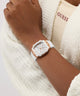 Hand wearing a white GUESS Ladies White Rose Gold Tone Analog Watch with gold accents on a white background