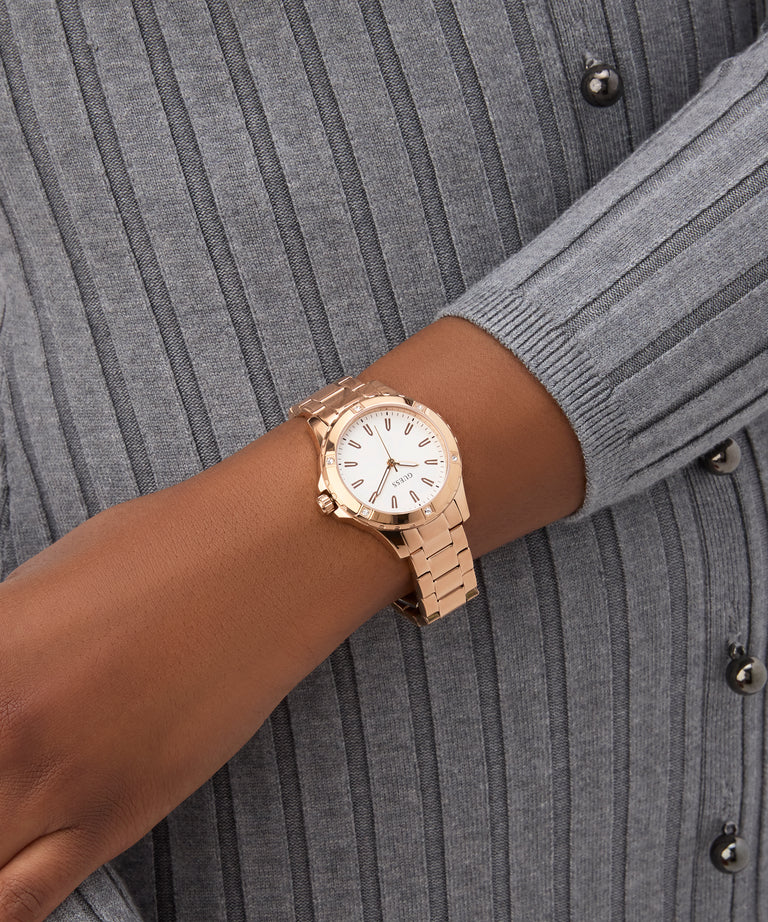GUESS Ladies Rose Gold Tone Analog Watch on a wrist with a gray ribbed sweater background