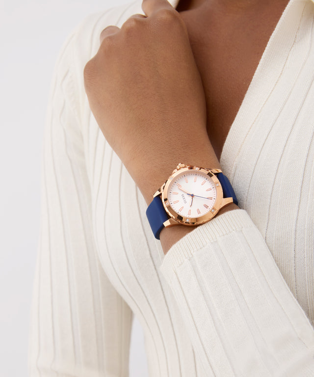 Rose gold watch with a blue strap on a wrist against a white background