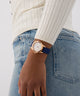 Person wearing a GUESS Ladies Blue Rose Gold Tone Analog Watch with a blue strap on a plain background
