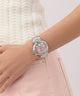 Wrist wearing a silver watch GW0950L1 with a pink face on a light background