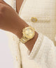 GUESS Ladies Gold Tone Multi-function Watch on a wrist with a textured cream-colored jacket