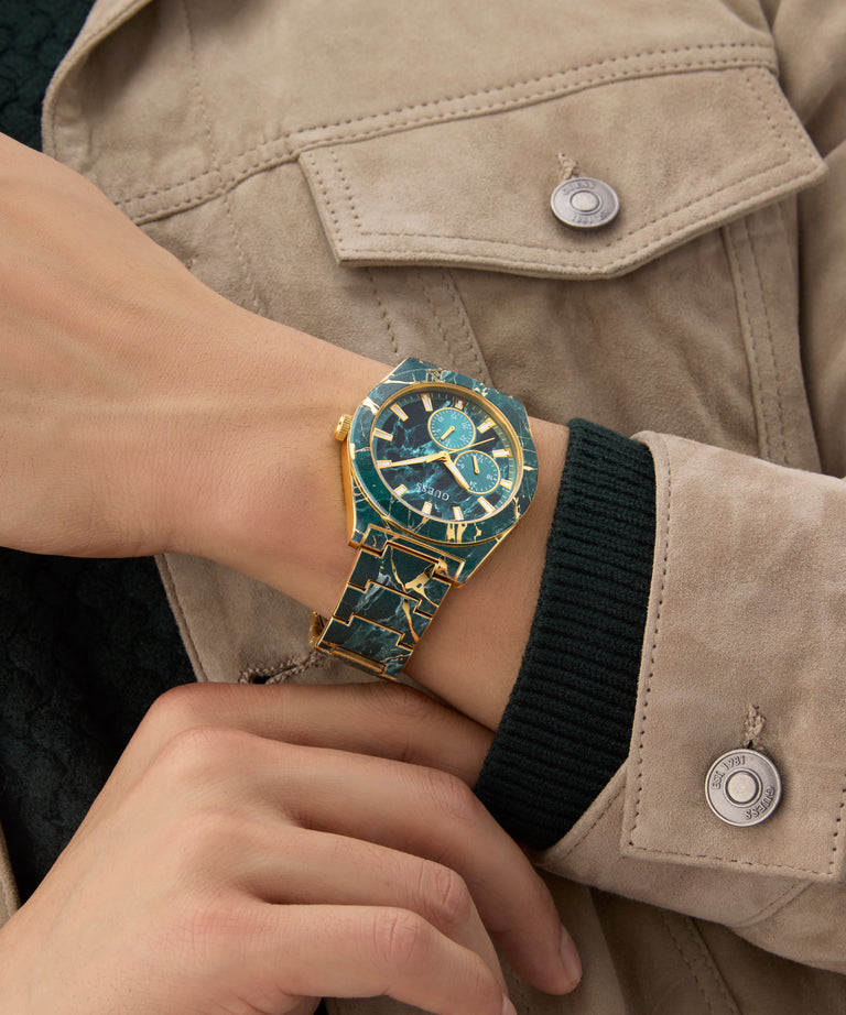 Close-up of a wrist wearing a gold and blue watch with a beige jacket.