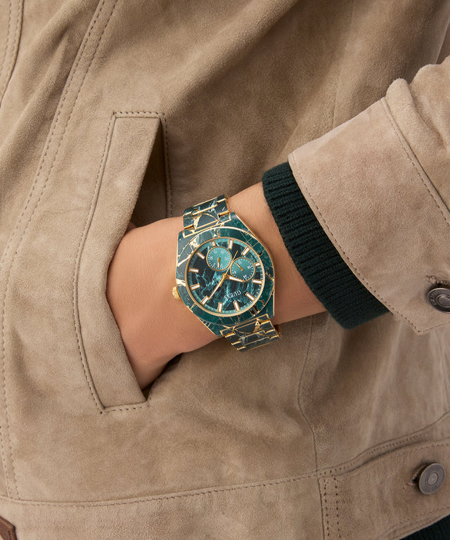 Close-up of a person wearing a turquoise and gold watch GW0953G1 on a beige jacket.