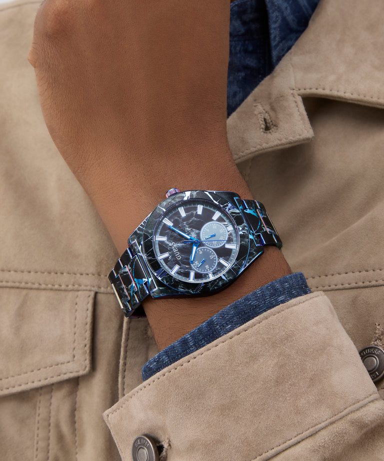 Person wearing a GUESS Mens Black Multi-function Watch with a detailed face and textured strap on a beige jacket.