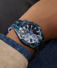 GUESS Mens Black Multi-function Watch with a detailed face on a person's wrist, wearing a dark jacket and light-colored shirt.