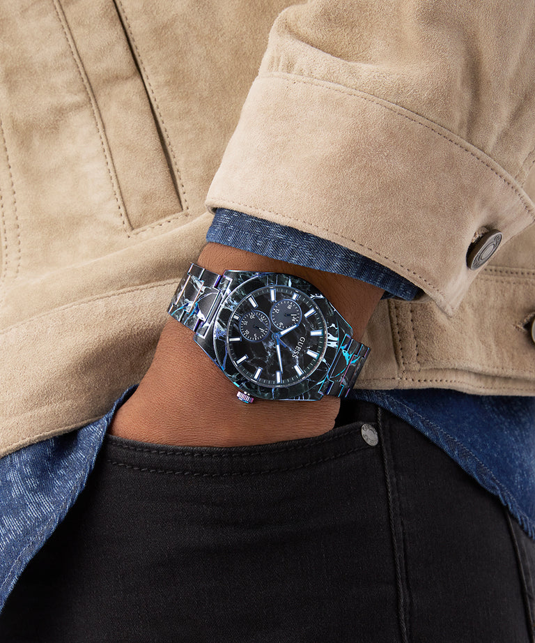 Close-up of a person wearing a silver GUESS Mens Black Multi-function Watch with a beige jacket and blue shirt.