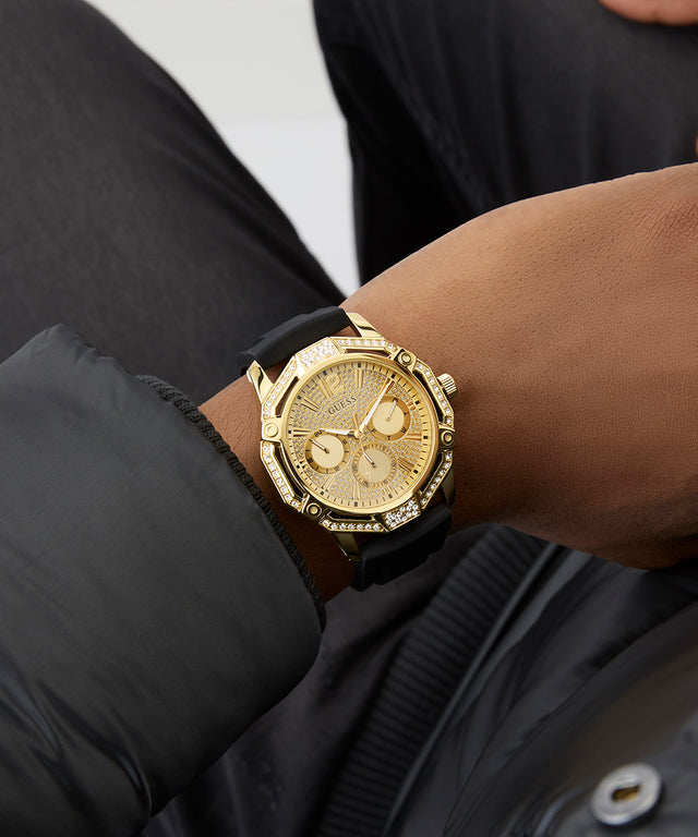 Gold GUESS Mens Black Gold Tone Multi-function Watch with black strap worn on a wrist against a dark background