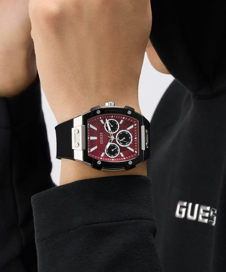 Person wearing a Guess watch with a red face and black strap.