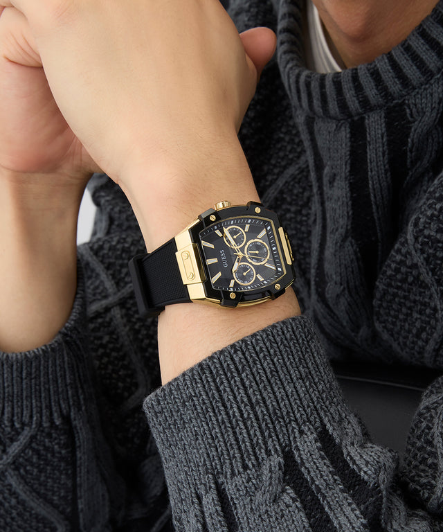 Gold and black watch on a person's wrist with a dark sweater GUESS Mens Black Gold Tone Multi-function Watch GW0956G2