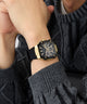 Gold and black watch on a person's wrist with a dark sweater GUESS Mens Black Gold Tone Multi-function Watch GW0956G2