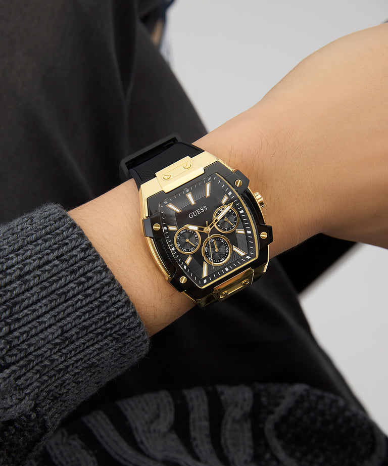 Gold and black watch on a wrist with a blurred background GUESS Mens Black Gold Tone Multi-function Watch GW0956G2