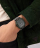 Person wearing a dark green jacket with a watch on their wrist